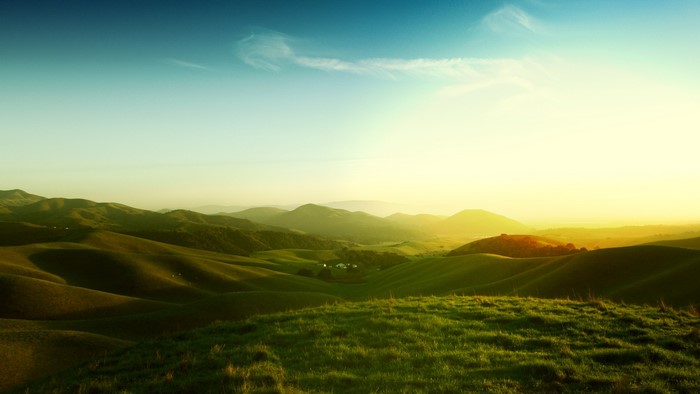 Rolling green hills under a bright sky at sunset
