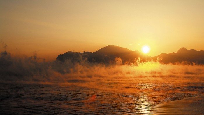 Sunrise over misty mountains and water