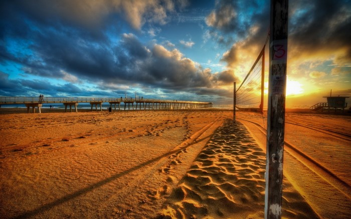 Beach volleyball net at sunset with pier and lifeguard tower