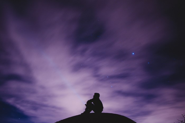 Silhouette of a person sitting under a starry purple sky