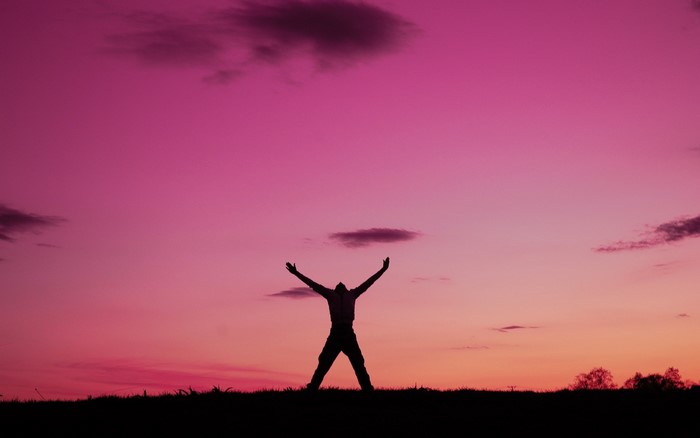 Silhouette of a person with arms raised against a pink sky