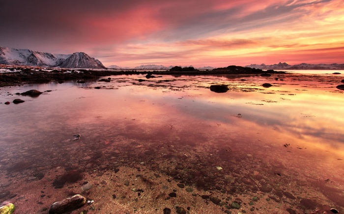 Sunset over a rocky coastline with snow-capped mountains