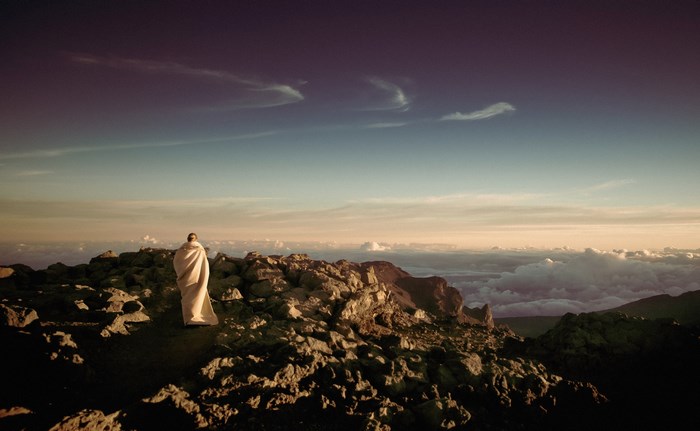 Person wrapped in a blanket on a rocky mountain peak
