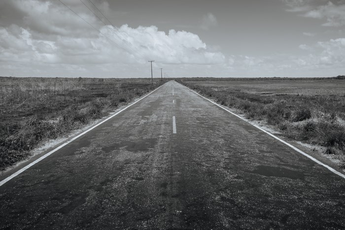 Black and white image of a long, empty road stretching to the horizon.