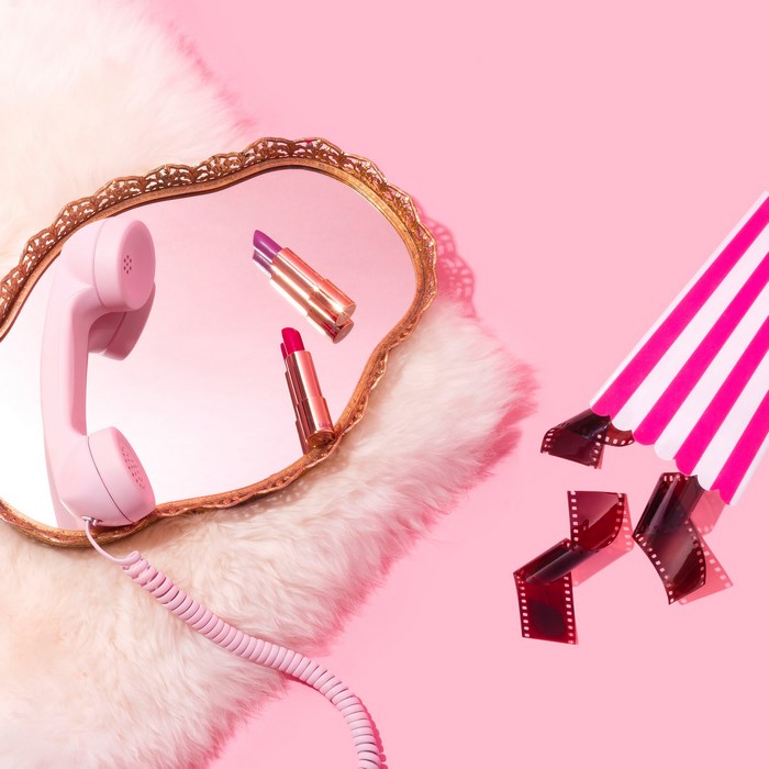 Pink telephone, lipsticks, and film reels on pink background