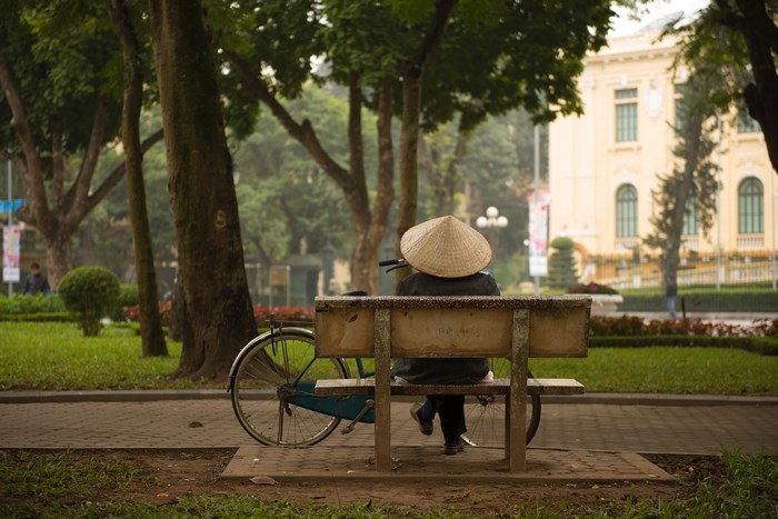 Person in conical hat on park bench with bicycle
