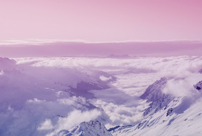 Snowy mountain range above clouds with pink sky