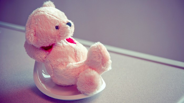Pink teddy bear sitting on a white saucer