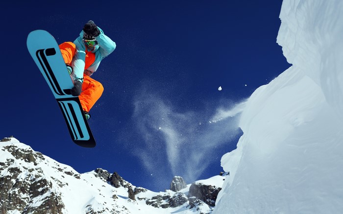 Snowboarder jumping off a snowy mountain cliff