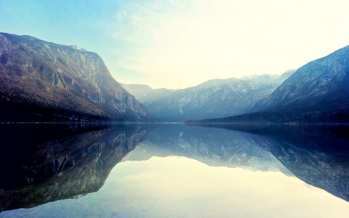 Mountains reflected in a calm lake under a bright sky