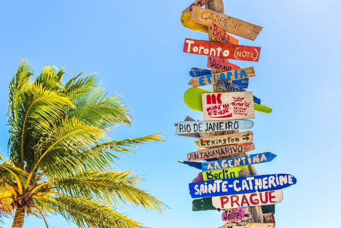 Directional signpost with destinations and a palm tree