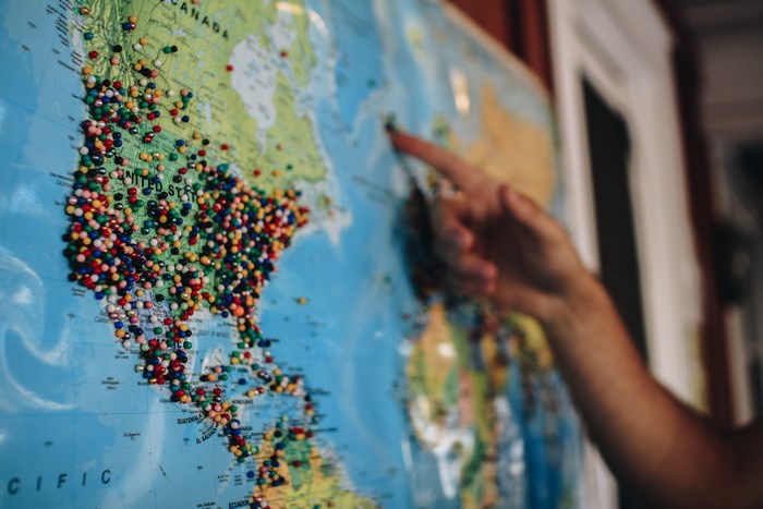 Hand pointing at a world map covered in pins
