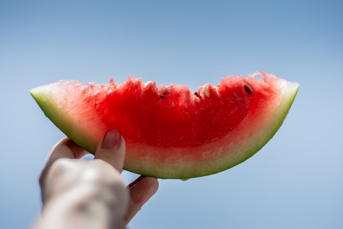Hand holding a slice of watermelon against a blue sky