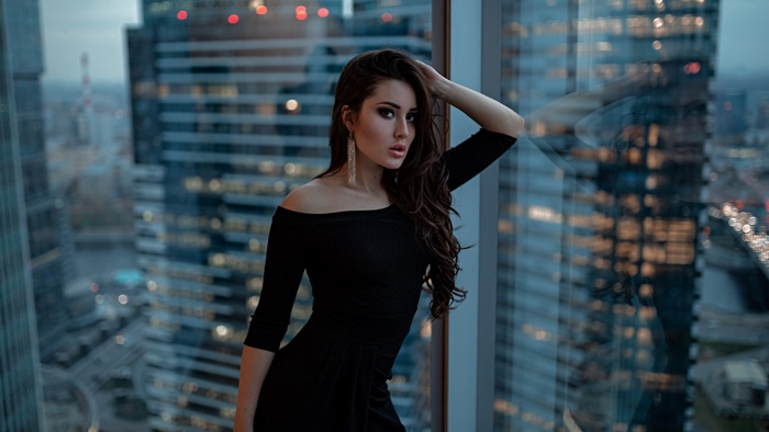 Woman in black dress by window with city view