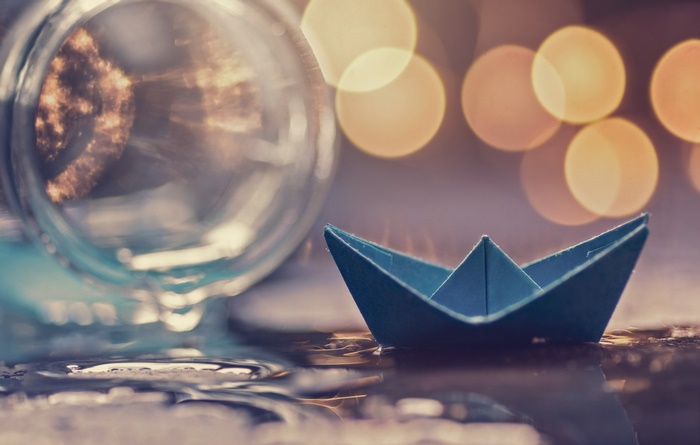 Blue origami paper boat in water with bokeh lights