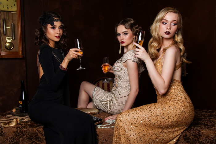 Three women in vintage dresses holding champagne glasses