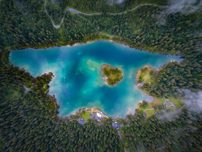 Aerial view of a heart-shaped island in a turquoise lake surrounded by a forest