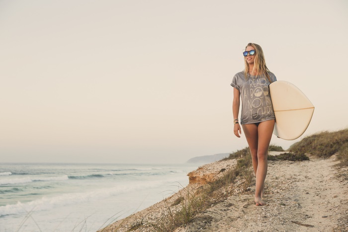 Woman with surfboard walking on beach path
