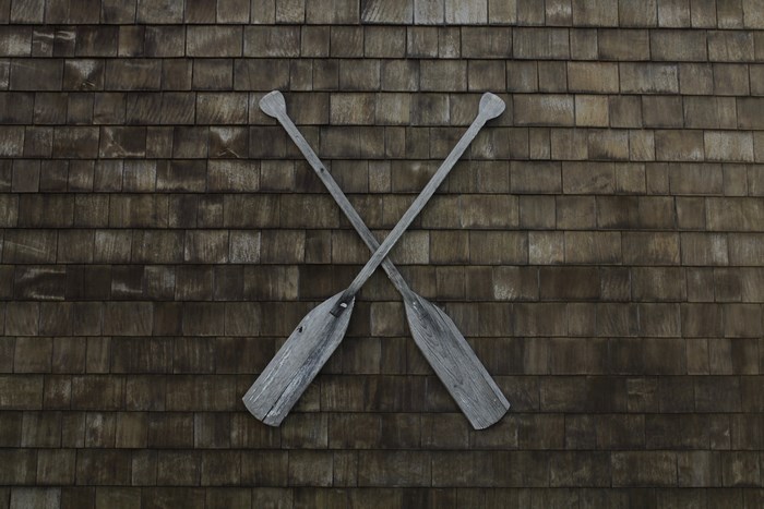 Two wooden oars crossed on a shingled wall