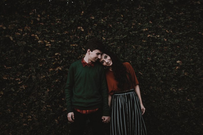 Couple holding hands in front of a leafy bush
