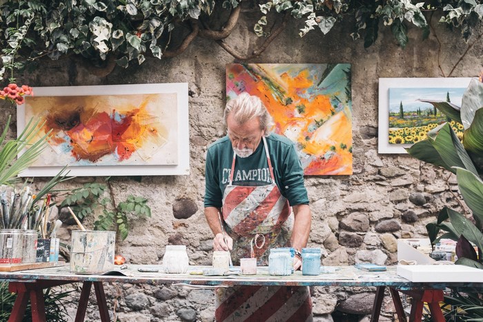 Artist painting outdoors with artwork on stone wall