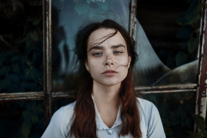 Woman with freckles and long hair in front of broken window