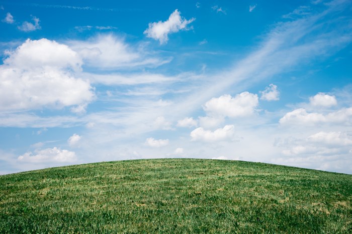 Green hill under a blue sky with clouds