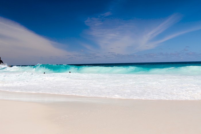 Turquoise wave crashing on a sandy beach under a blue sky