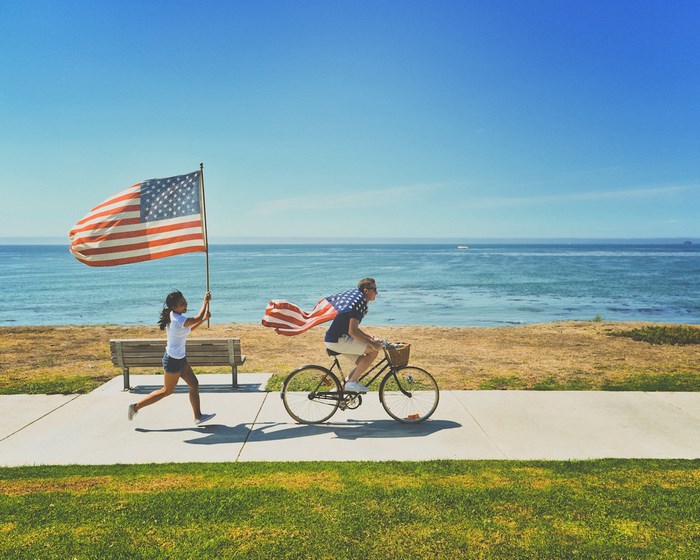 Girl runs with American flag, man cycles by ocean