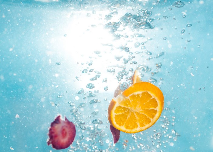 Orange and strawberry slices sinking in water with bubbles