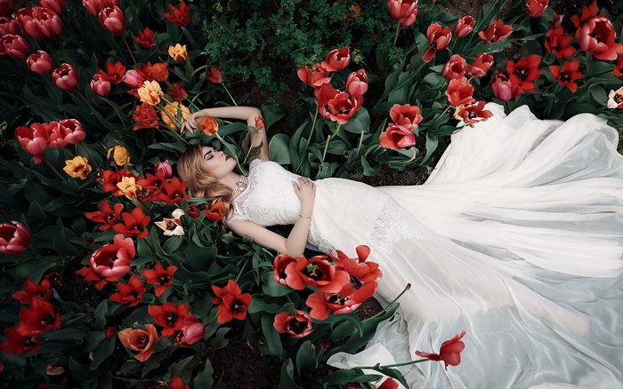 Woman in white dress lying in red tulips