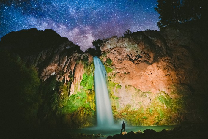 Man stands by waterfall under the Milky Way