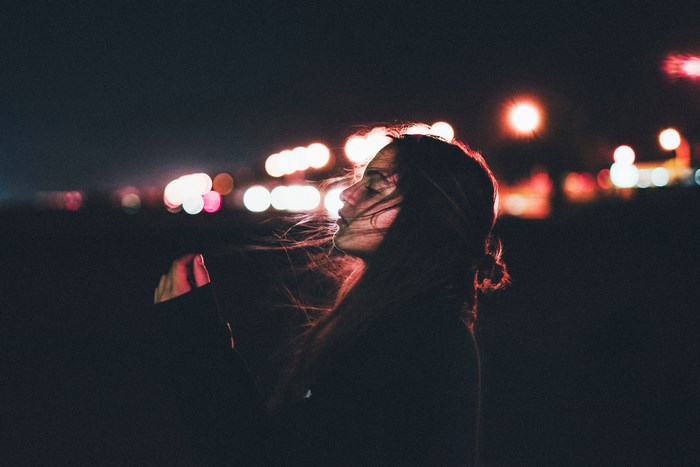 Woman with hair blowing in the wind at night with city lights