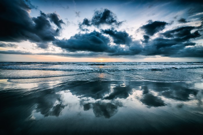 Beach with dramatic clouds and reflection at sunset