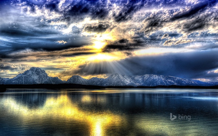 Sunbeams over snow-capped mountains and a lake