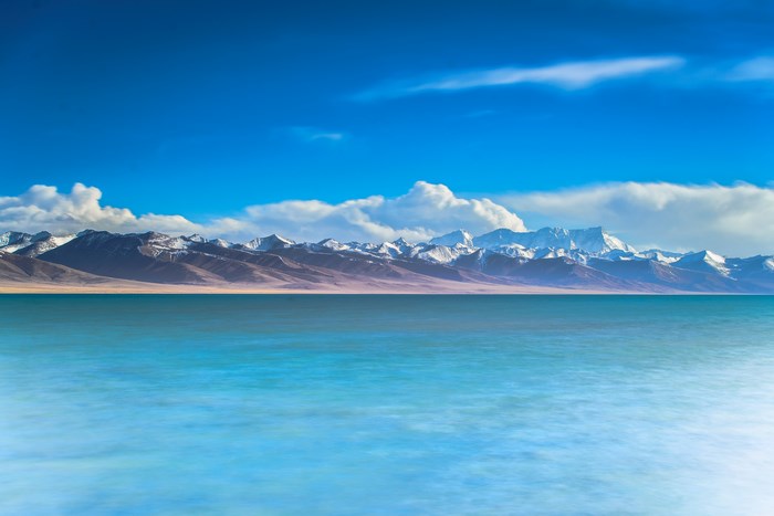 Snow-capped mountains over a tranquil lake under a blue sky