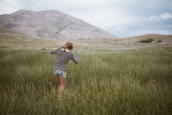 Girl walking through tall grass with mountains in background