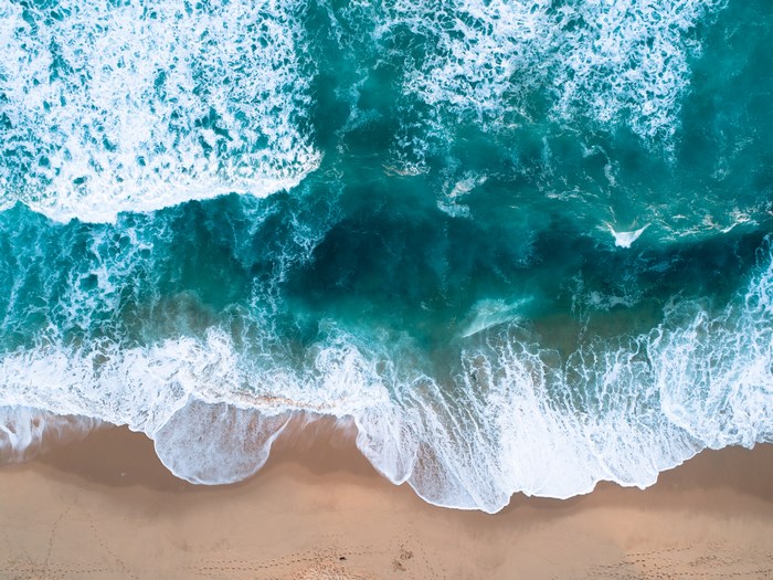 Aerial view of ocean waves crashing on a sandy beach in Australia