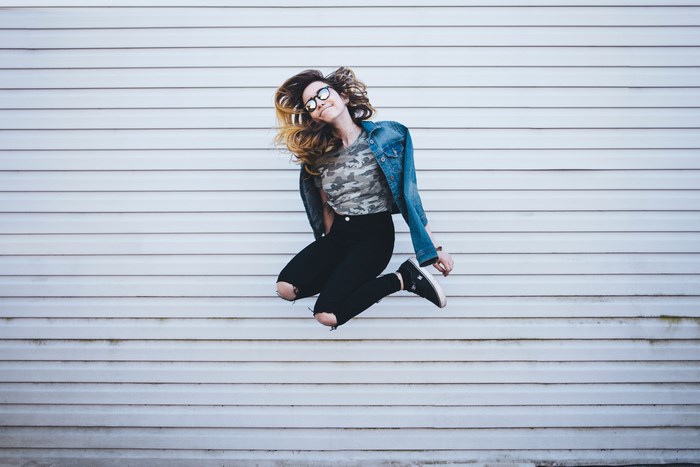Woman in denim jacket jumping in front of a wall