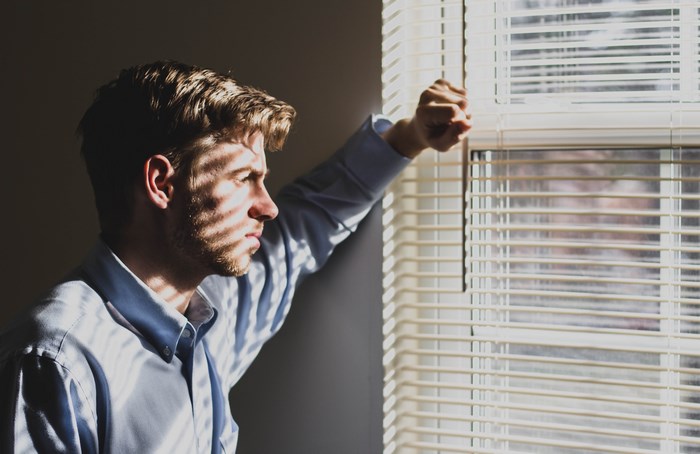 Man looking out window through blinds