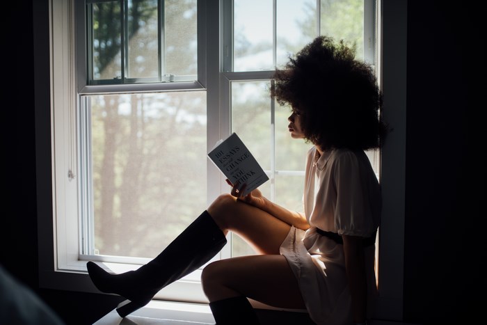 Woman with afro reading a book by the window