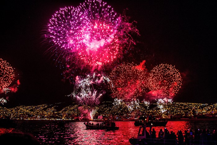 Fireworks over a city at night with boats on the water