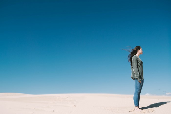 Woman standing on sand dunes under blue sky