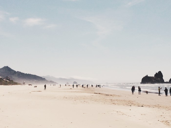 People walking on a sandy beach with rock formations