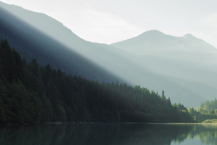 Sunlight rays over a forest lake and mountains