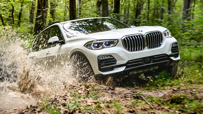 White BMW X5 driving through a muddy forest stream