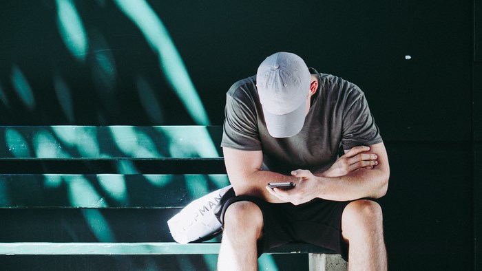 Man in baseball cap looking at phone on steps