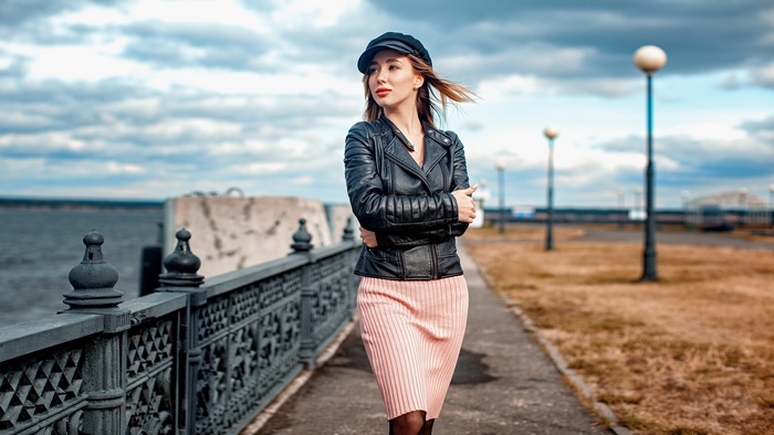 Woman in leather jacket and cap walking by the water