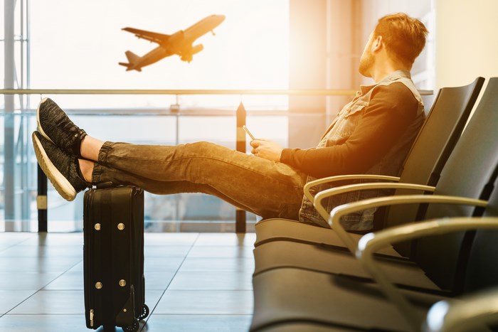 Man waiting at airport with suitcase and plane flying