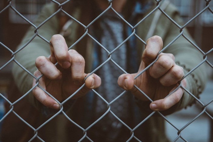 Person gripping a chain-link fence